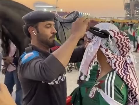 بالفيديو.. رجل أمن قطري يساعد مشجعة مكسيكية على لبس «الغترة»